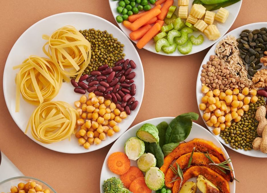 A vibrant mix of legumes, vegetables, nuts, and pasta arranged on white plates showcasing a balanced, healthy diet.